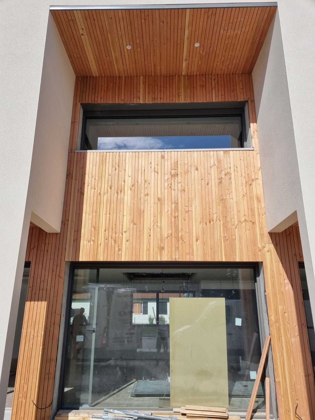 Façade avec des lattes de bois autour des encadrements de fenêtres et de portes ; murs blancs.