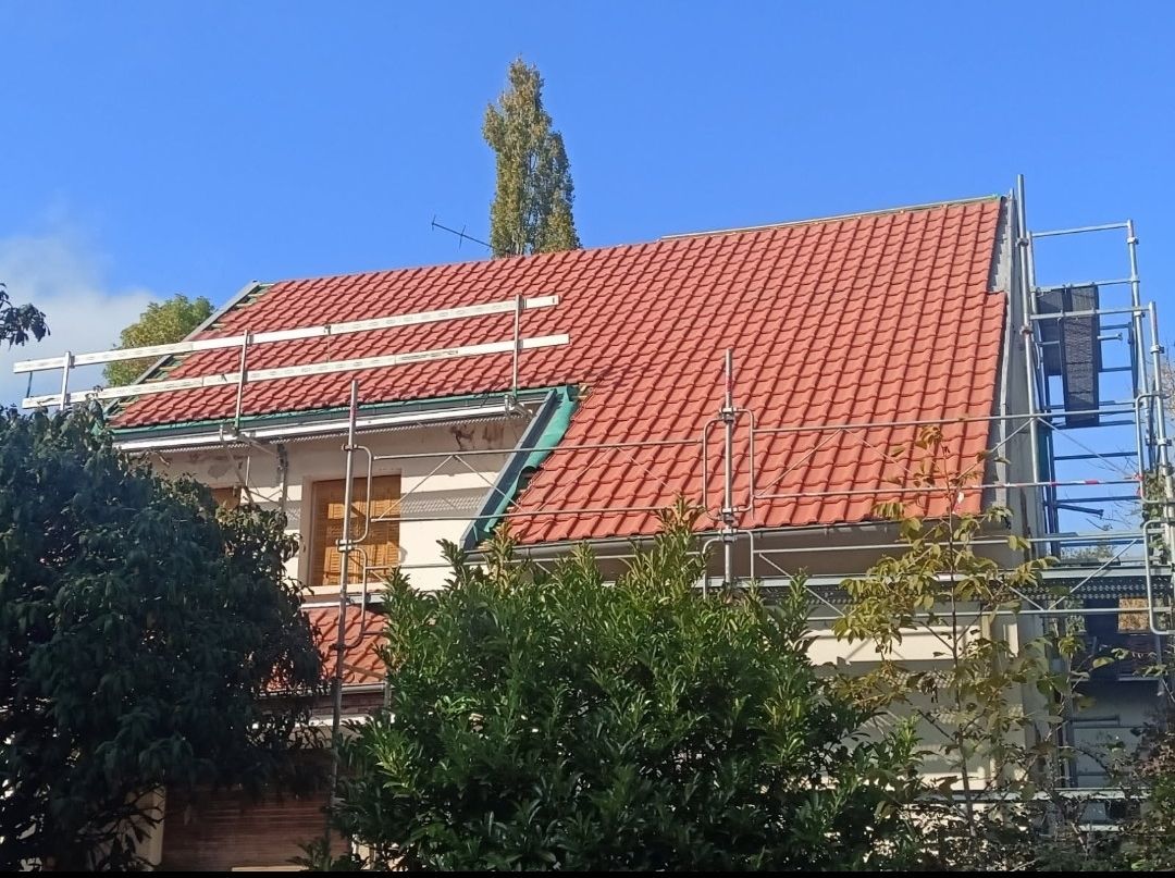 Maison en construction avec toit de tuiles rouges ; des échafaudages entourent le bâtiment.