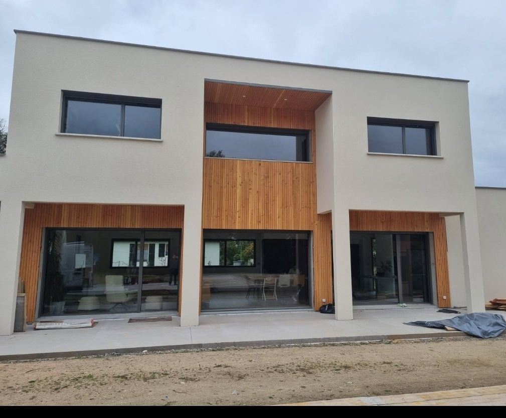 Maison moderne à deux étages avec une façade claire et des éléments en bois autour des fenêtres et de l'entrée.