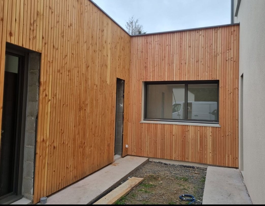 Vue extérieure d'un bâtiment avec bardage en bois, fenêtre et allée en béton.