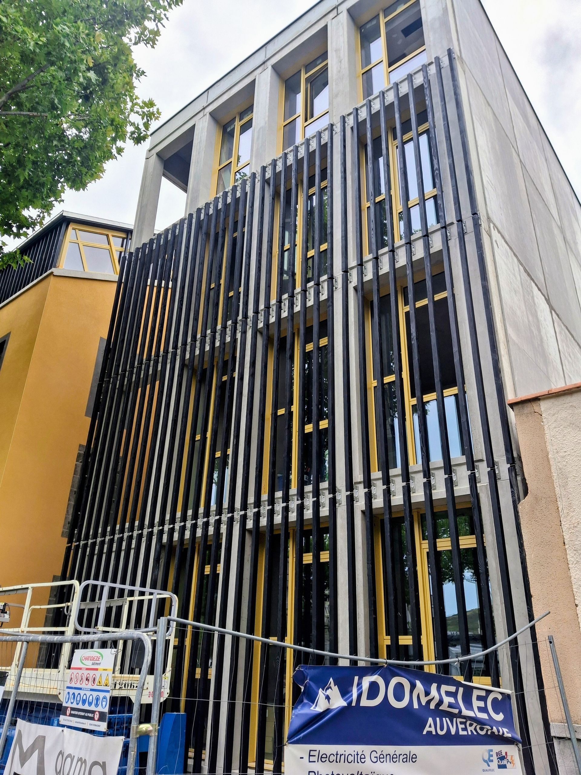 Immeuble à plusieurs étages en construction ; façade à lames verticales noires et dorées.