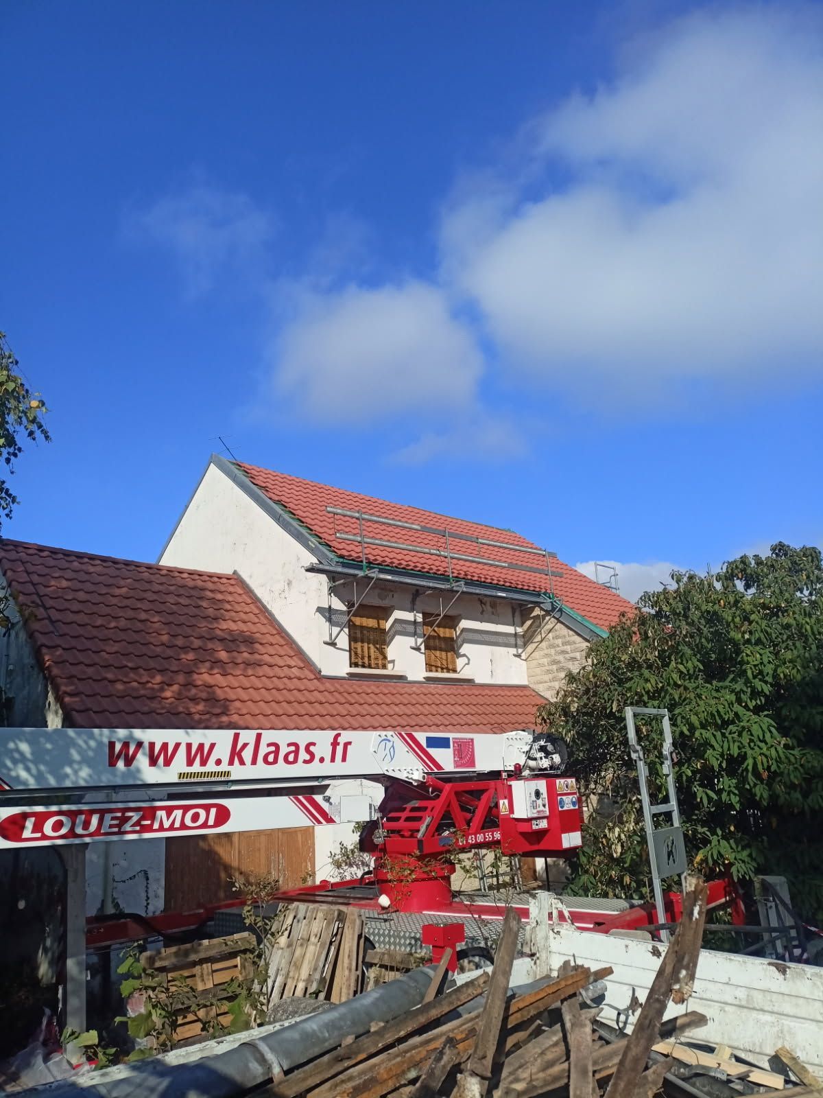 Grue rouge à côté d'une maison blanche au toit rouge sous un ciel bleu.