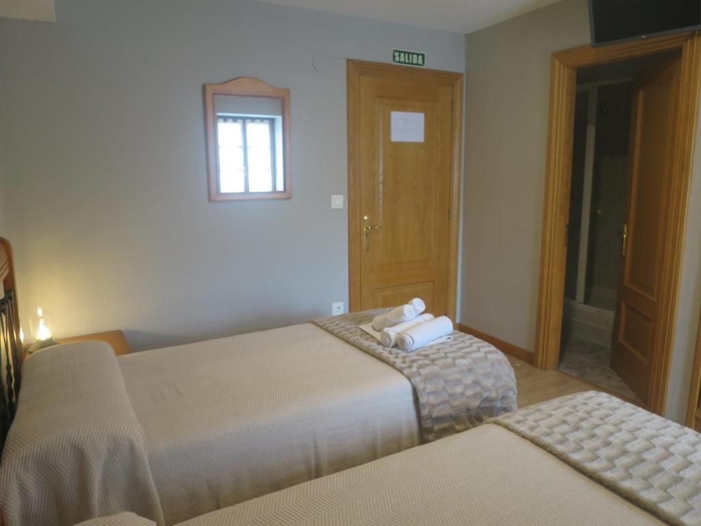 Camas individuales en una habitación de hotel con sábanas de color beige, una puerta al baño y un espejo.