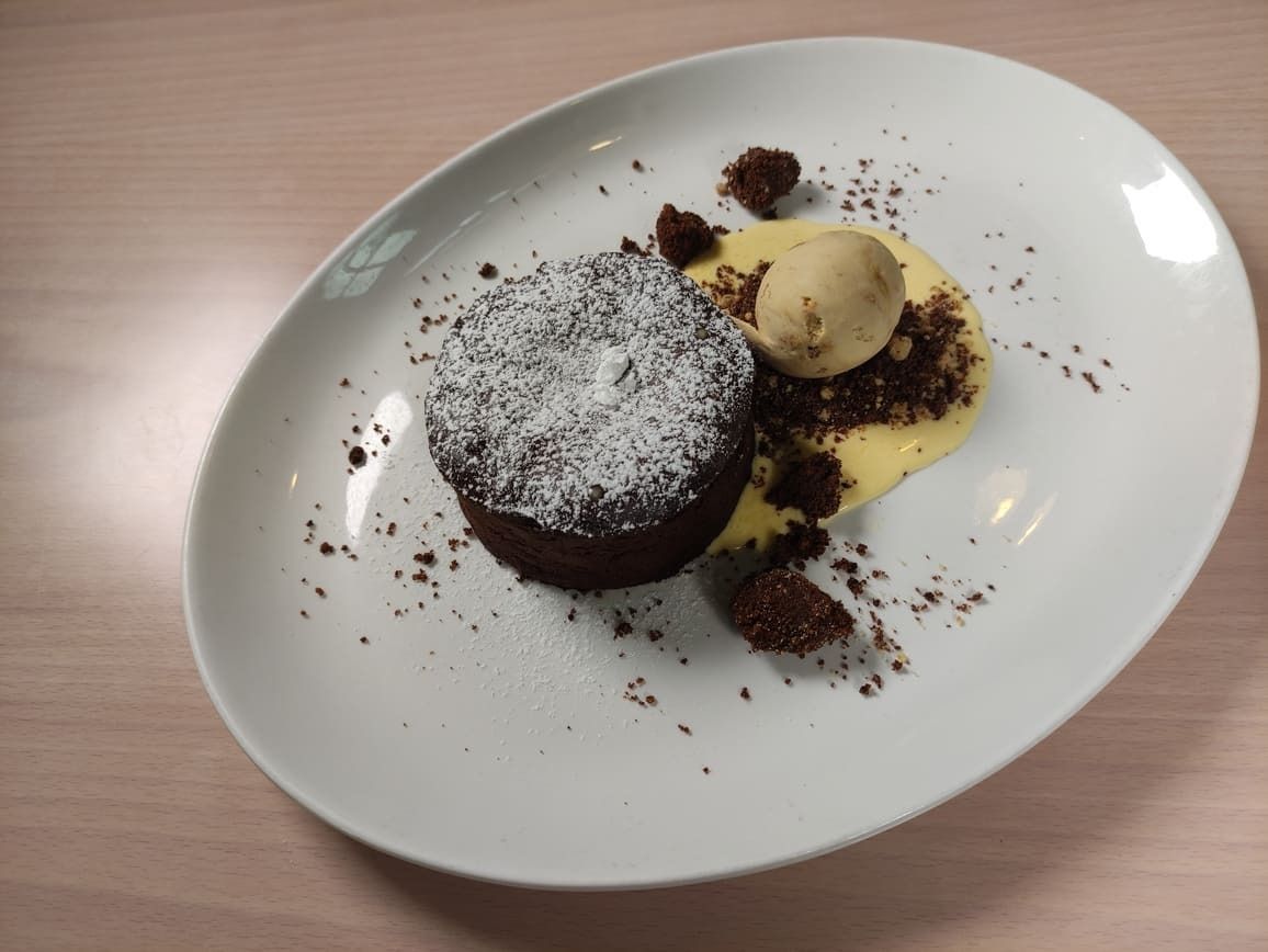 Pastel de lava de chocolate con salsa de vainilla, helado y migas de chocolate en un plato ovalado blanco.