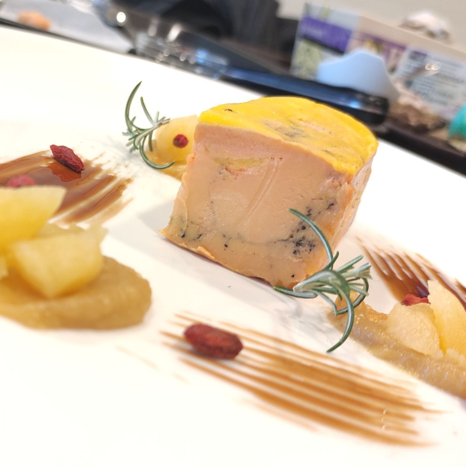 Foie gras con salsa, fruta y hierbas en un plato blanco.