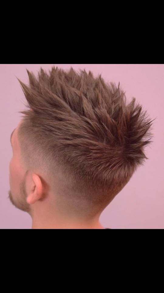 Un hombre con un peinado mohawk está parado frente a una pared rosa.