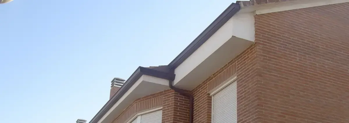 Un edificio de ladrillo con molduras blancas y techo oscuro bajo un cielo azul claro.