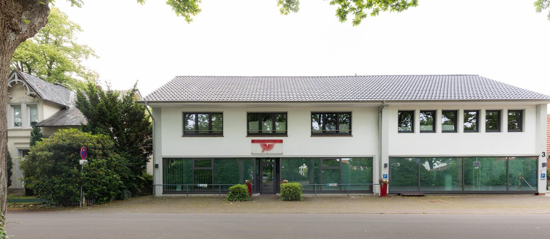 Kleines weißes Gebäude mit grünen Zierelementen und Ziegeldach neben einer Straße