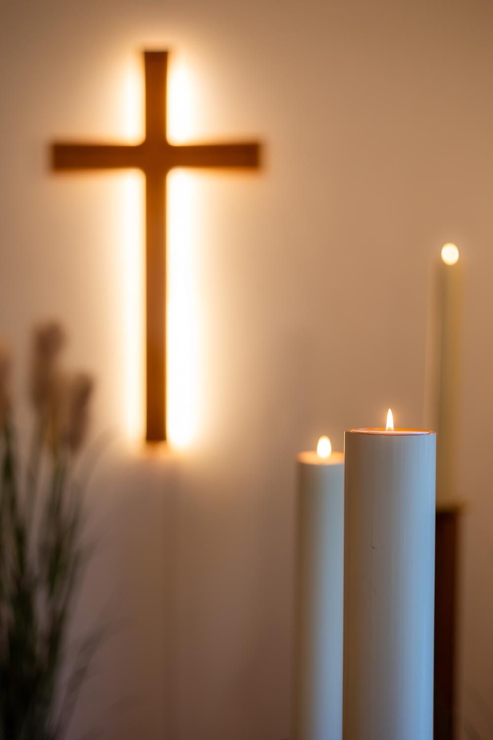 Leuchtendes Kreuz an einer Wand mit brennenden Kerzen im Vordergrund