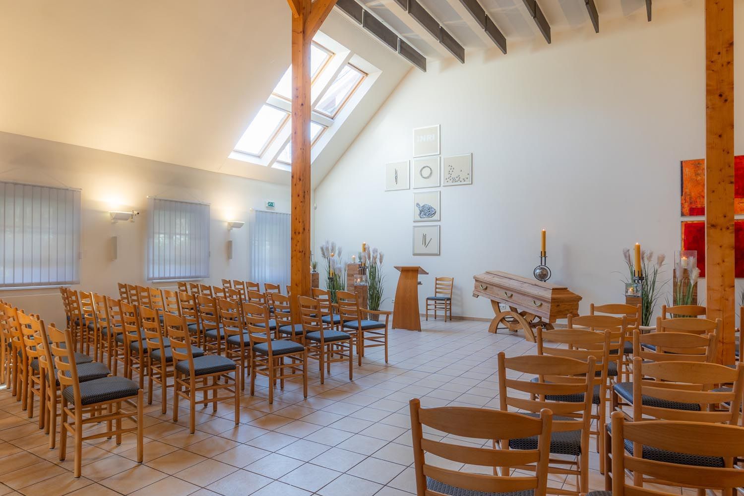 Ein leerer Kirchensaal mit Reihen von Holzstühlen, weißen Wänden und einem Oberlicht über dem gefliesten Boden.
