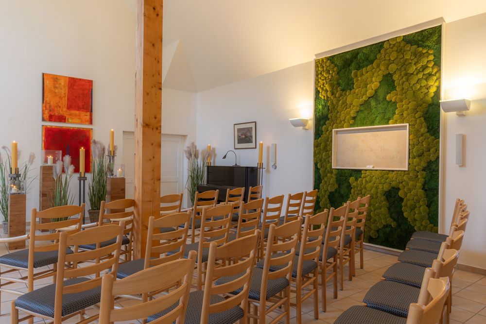 Kircheninneres mit Reihen von Holzstühlen, Altarkerzen und einer grünen Blumenwand hinter der Kanzel