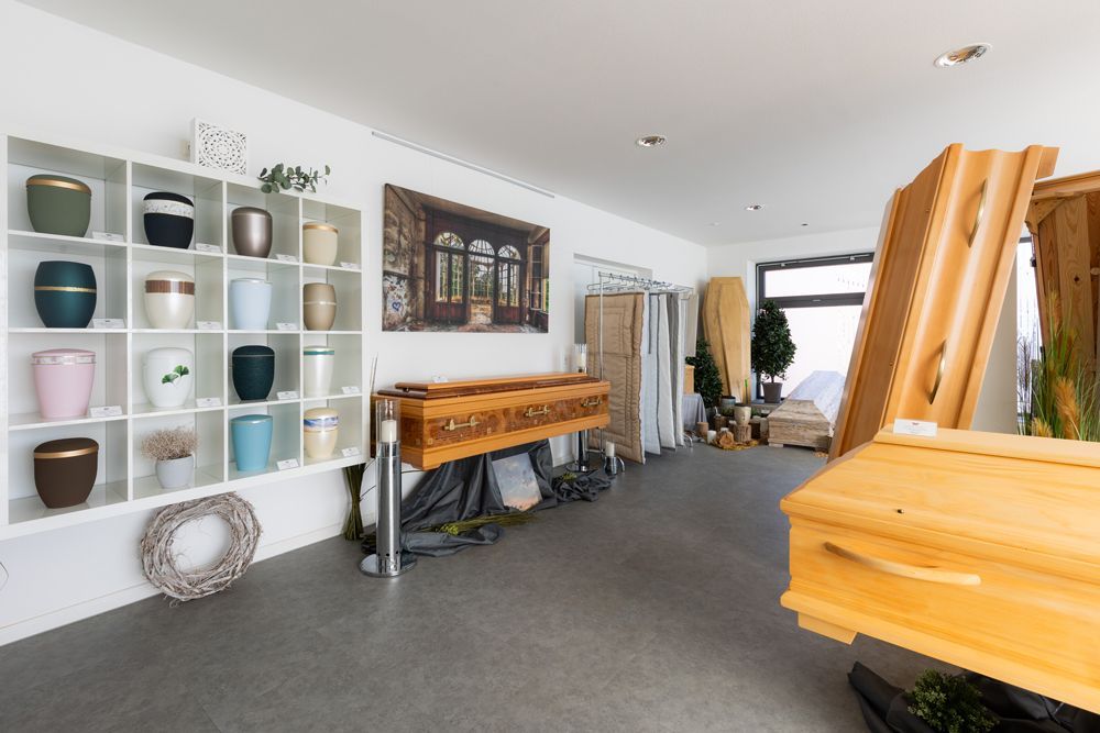 Heller Ausstellungsraum mit Regalen voller Keramiktöpfe, Holztischen und Zimmerpflanzen auf grauem Teppichboden.