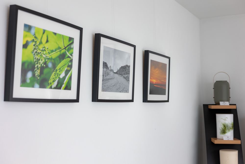 Gerahmte Drucke an einer weißen Wand neben einem schwarzen Regal mit einer Pflanze und Deko.