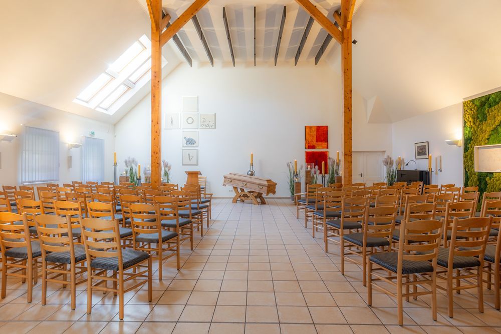 Leere Kapelle mit Reihen von Holzstühlen, die einem kleinen Altar unter freiliegenden Balken und Oberlichtern zugewandt sind.