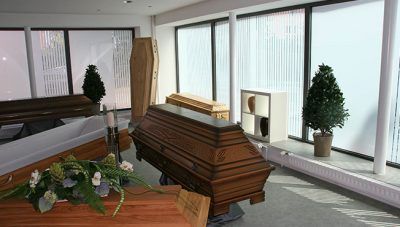 Zwei polierte Holzsärge in einem hellen Trauerraum mit Blumen und Topfpflanzen