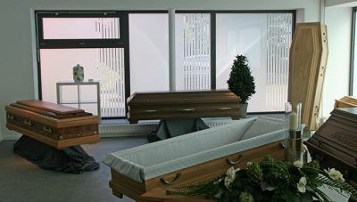 Trauerraum mit drei Särgen und Blumengestecken in der Nähe großer Fenster