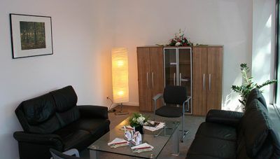 Modernes Wohnzimmer mit schwarzen Sofas, Couchtisch aus Glas, Stehlampe und Holzschrank.