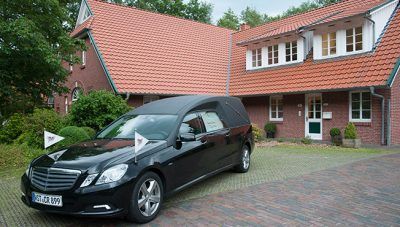 Ein schwarzer Mercedes-Minivan parkt in einer Einfahrt neben einem Backsteinhaus mit rotem Ziegeldach.