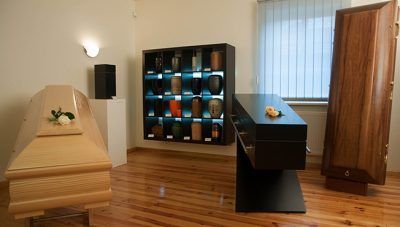 Museumsgalerie mit sargähnlichen Exponaten und einer zentralen Ausstellung farbenfroher Gefäße auf polierten Holzböden