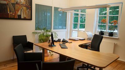 Moderner Konferenzraum mit Holztisch, schwarzen Stühlen und großen Fenstern mit Blick ins Grüne