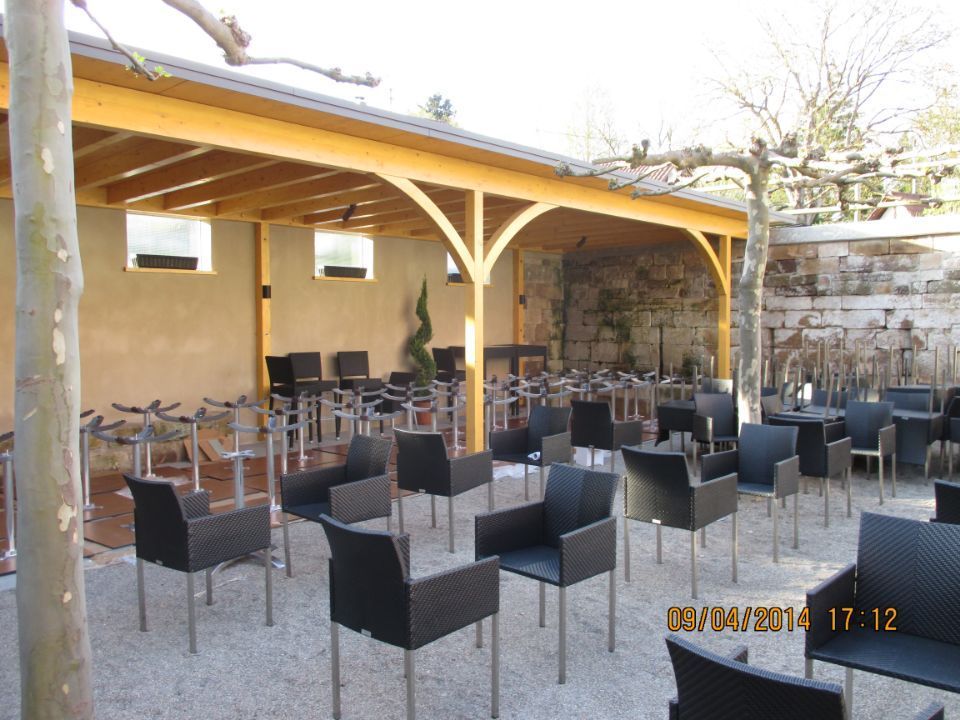 Innenhof mit hohen Stühlen, im Hintergrund eine Naturholzüberdachung einer Terrasse