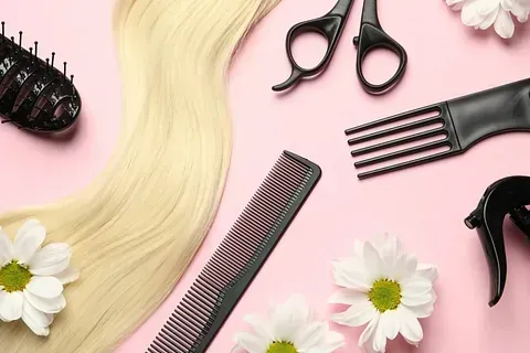 Un peine, unas tijeras, un cepillo y flores sobre un fondo rosa.