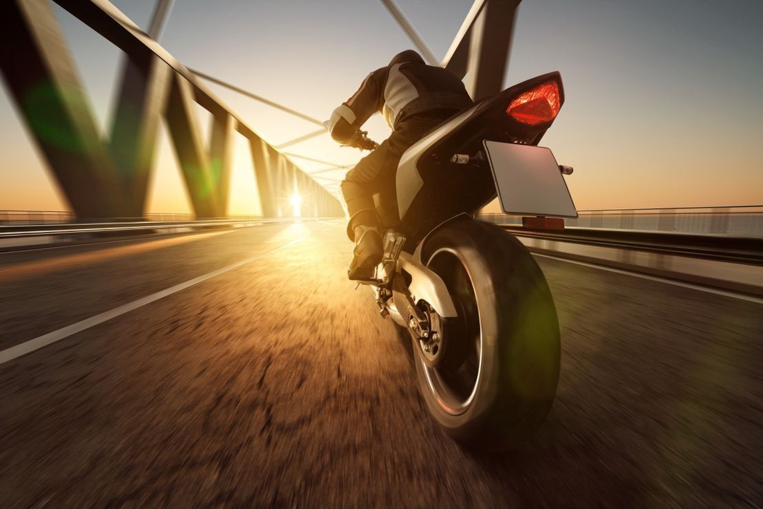 Una persona va en motocicleta por un puente al atardecer.