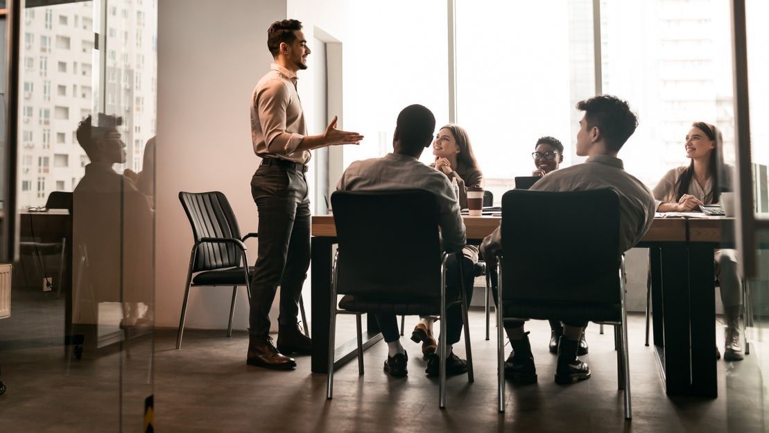 Un hombre está dando una presentación a un grupo de personas sentadas alrededor de una mesa.