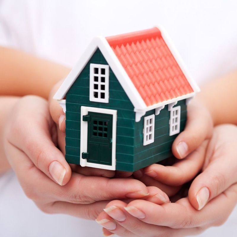 Una persona sostiene una pequeña casa verde con techo rojo.