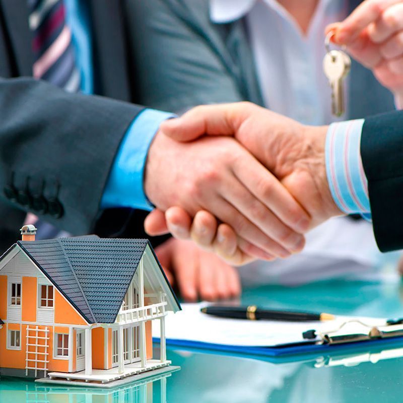 Dos personas se dan la mano con una casa modelo en primer plano