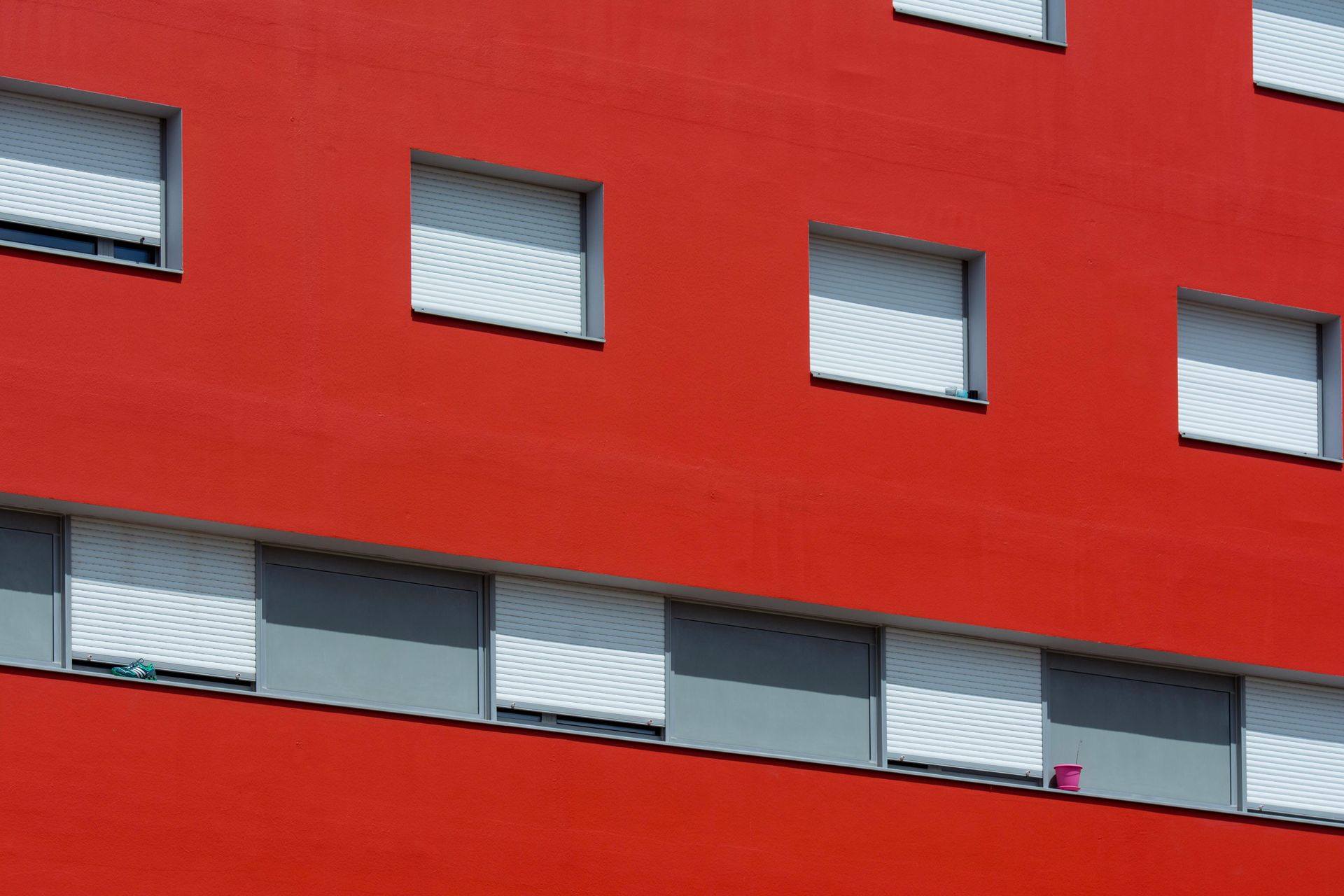 Una fachada de edificio de color rojo brillante con una cuadrícula de ventanas con contraventanas blancas