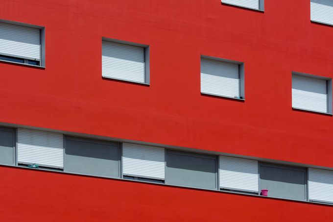 Una fachada de edificio de color rojo brillante con una cuadrícula de ventanas con contraventanas blancas