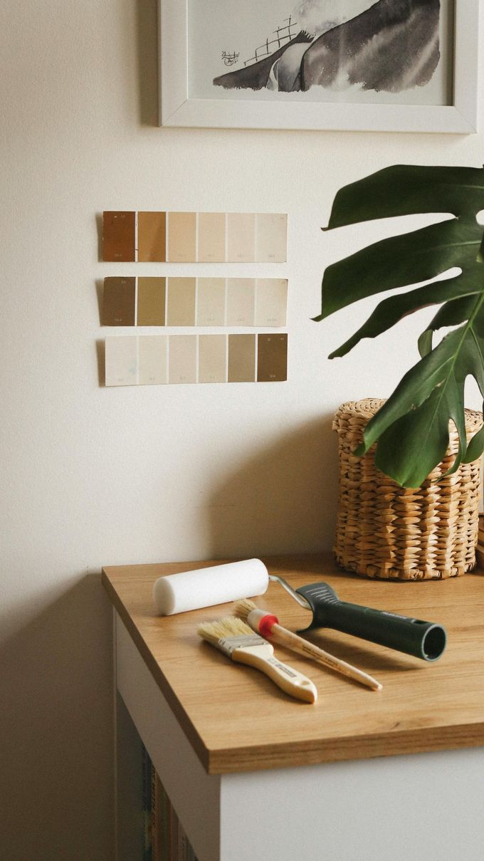 Muestras de pintura en tonos beige y marrón pegadas con cinta adhesiva a una pared junto a los materiales de pintura