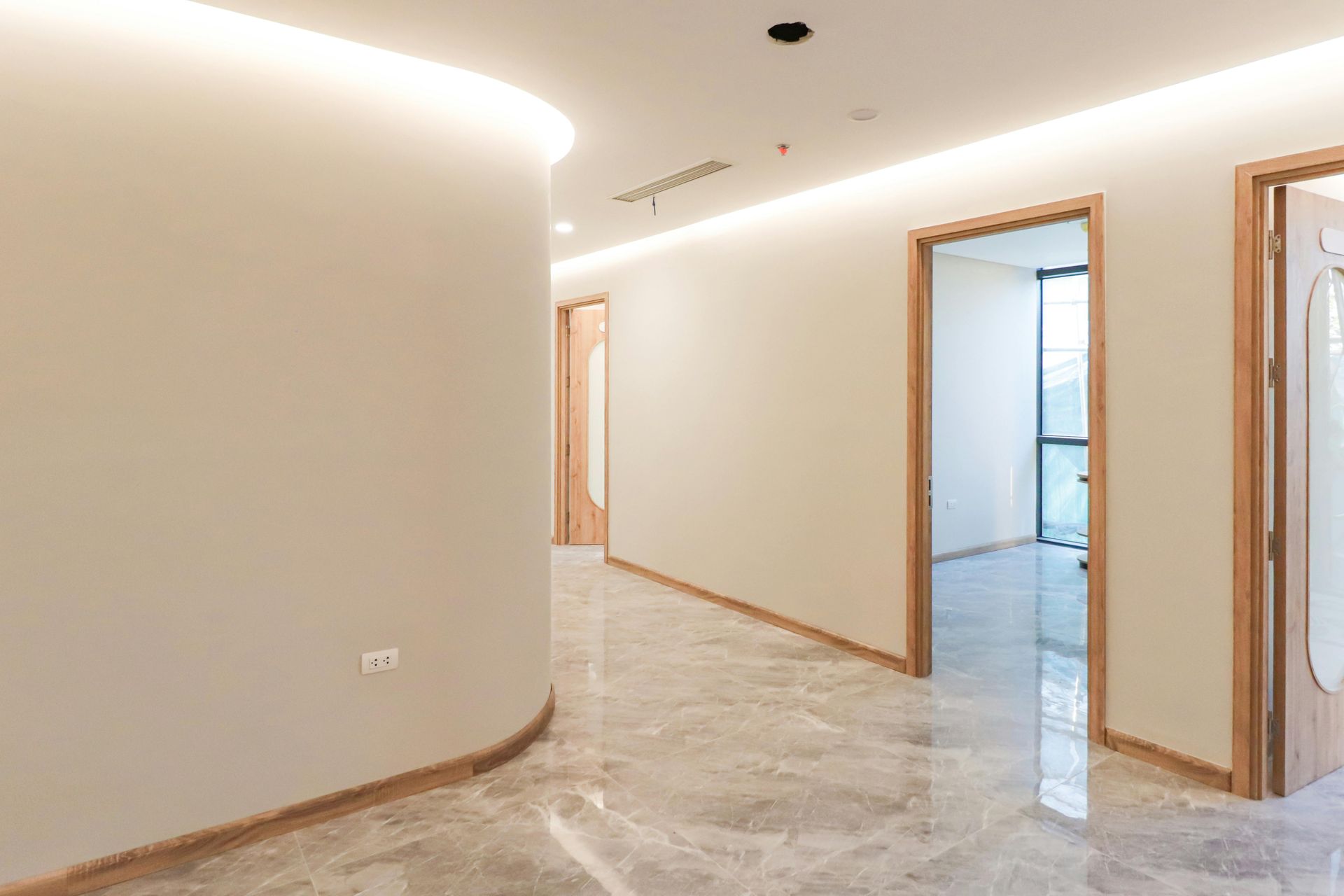 Un pasillo moderno y minimalista con paredes curvas de color beige, iluminación empotrada en el techo