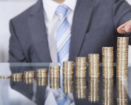 Hombre con traje agregando monedas a pilas crecientes de monedas.