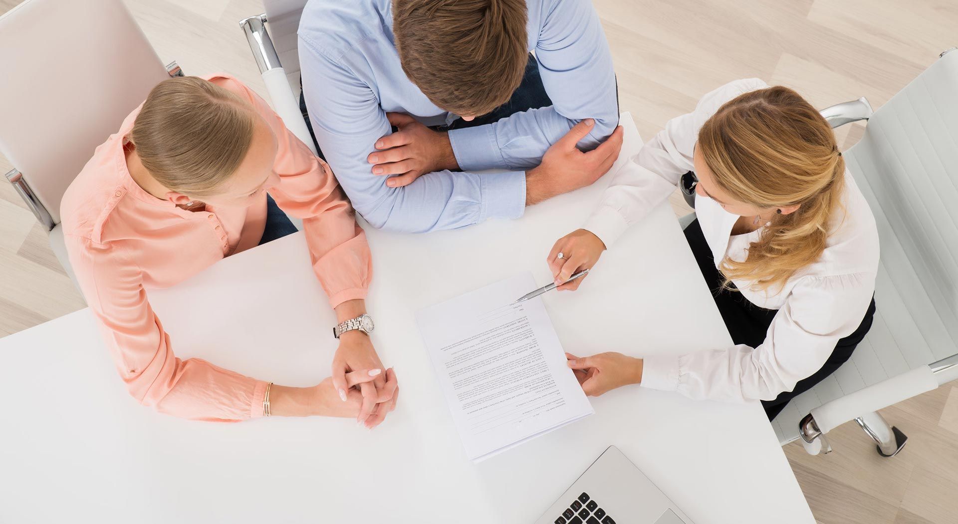 Vista aérea de tres personas en una mesa blanca, una de ellas señalando un documento.