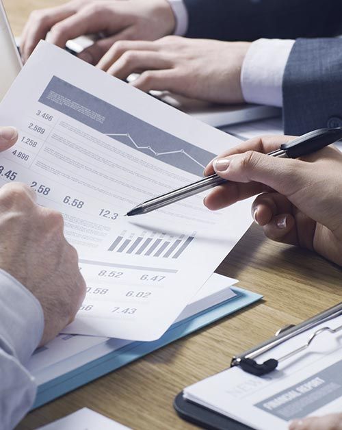 La gente sentada en un escritorio revisa datos financieros, señalando cuadros y gráficos.