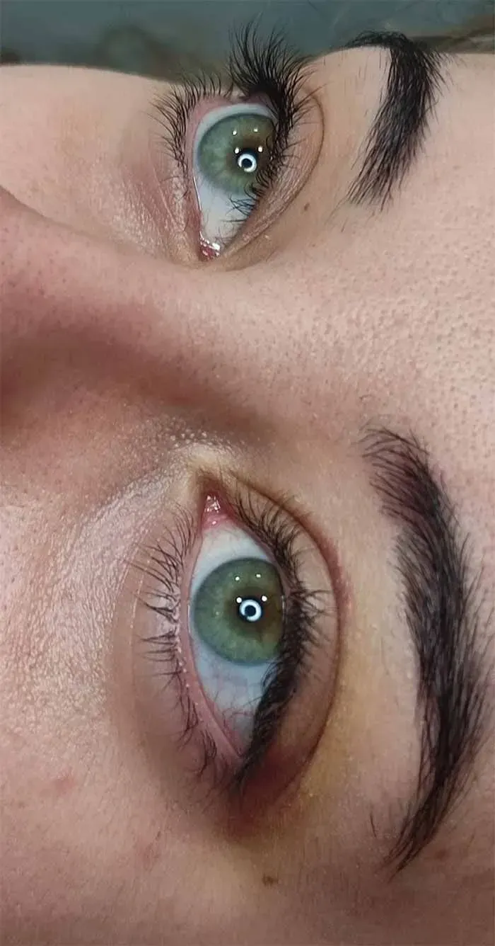 Primer plano del rostro de una persona. Sus ojos verdes miran hacia arriba. Tiene cejas oscuras y piel clara.