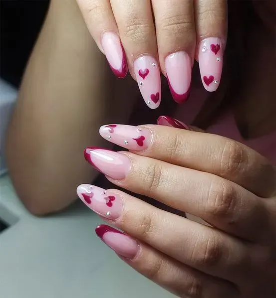 Uñas cuidadas, puntas francesas con diseños de corazones rojos y rosas y pedrería.