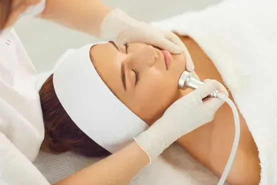 Mujer recibiendo un tratamiento facial en un spa. El técnico le coloca el dispositivo en la cara.
