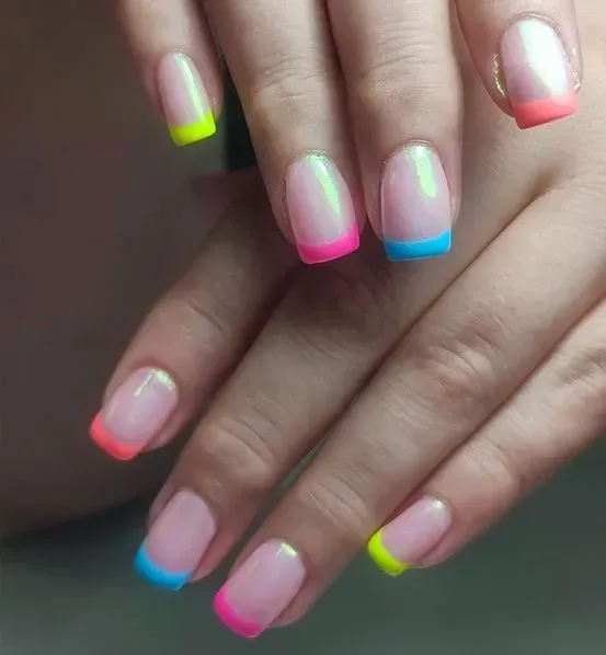 Primer plano de manos con uñas de color rosa claro y puntas de neón de colores: amarillo, rosa y azul.