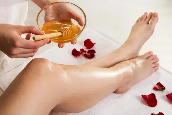 Piernas depiladas en un spa, con un recipiente con miel y pétalos de rosa.