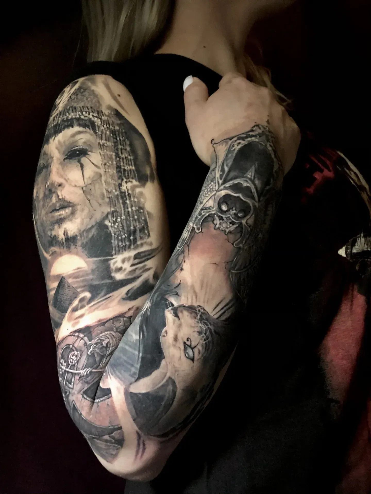 Tatuaje de mujer en el brazo con retrato, lobo y calavera. Sombreado en negro y gris.