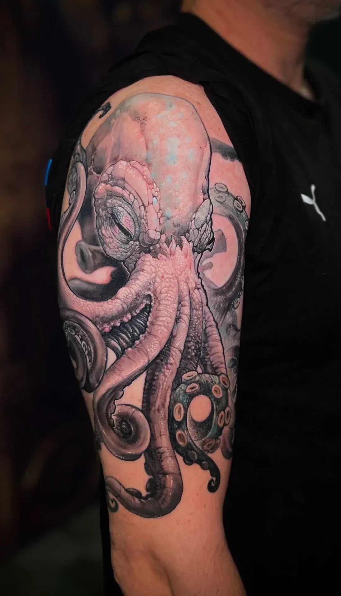 Tatuaje de pulpo negro y gris en la parte superior del brazo de una persona, con sombreado detallado y ventosas.