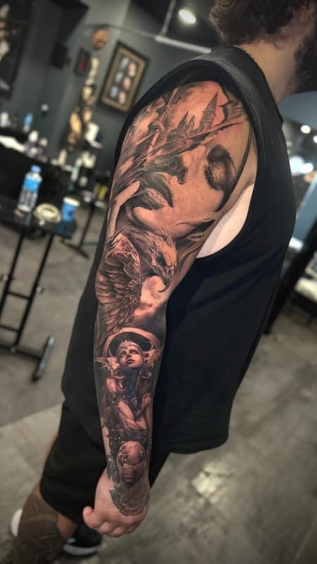 Primer plano del brazo tatuado de una persona que lleva una camiseta negra sin mangas, en el interior de una barbería o estudio.