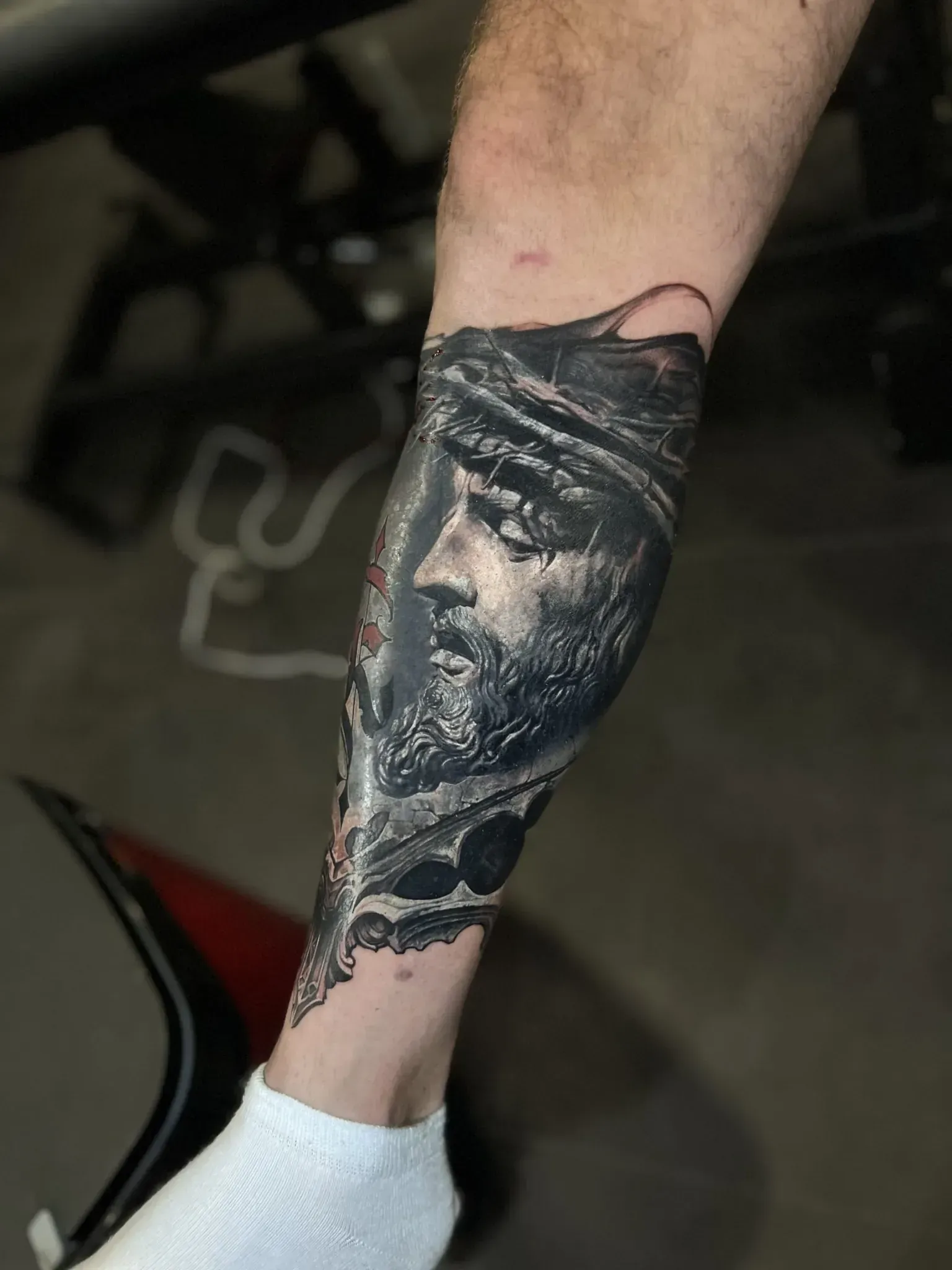 Tatuaje de la pierna de una persona con un retrato detallado en escala de grises de una figura con barba y corona.