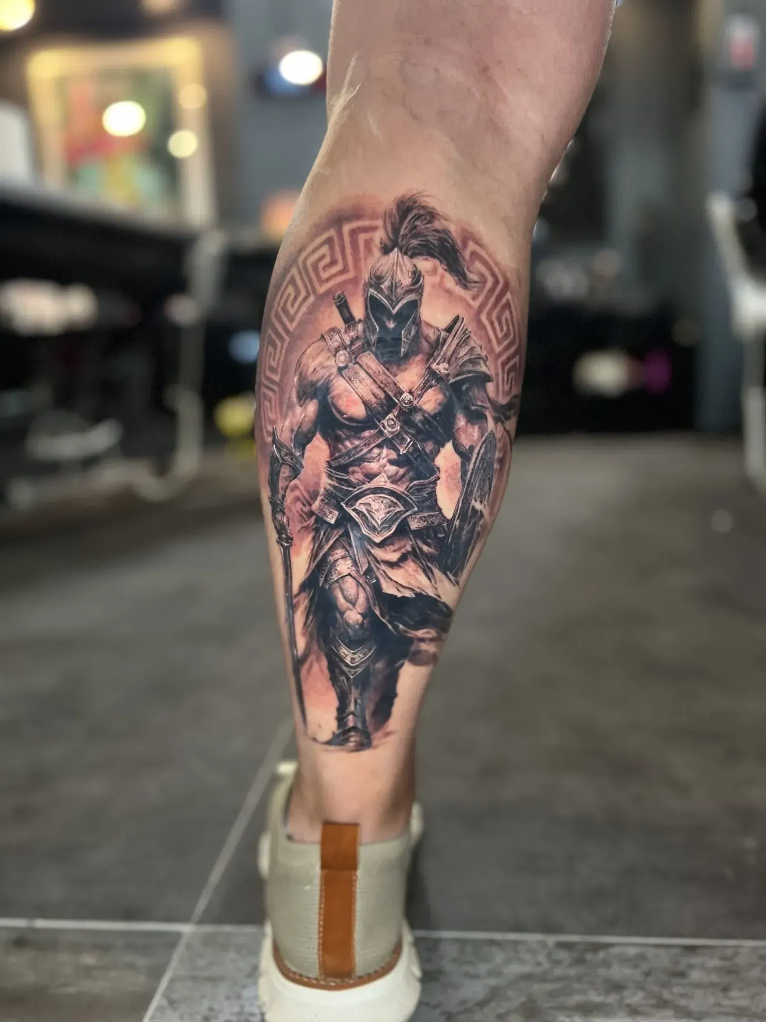 Tatuaje de un guerrero musculoso con armadura sosteniendo un arma.