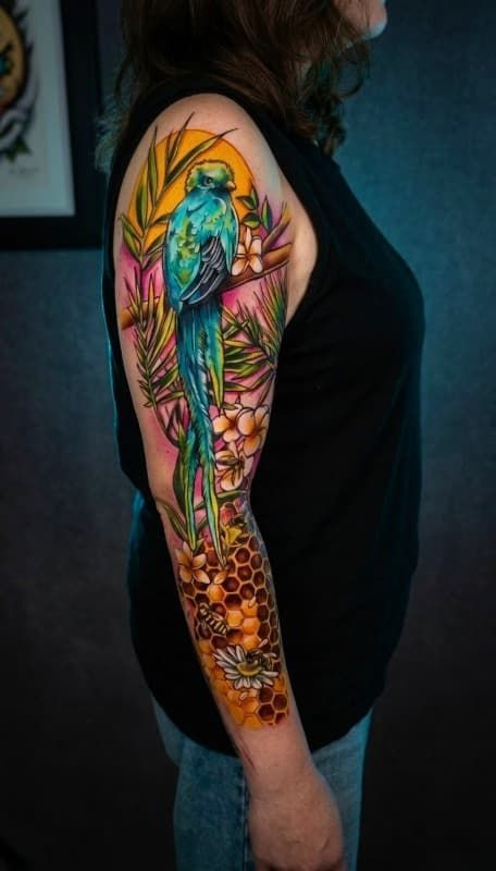 Tatuaje en la parte superior del brazo de una mujer con un pájaro colorido con motivos florales y geométricos.