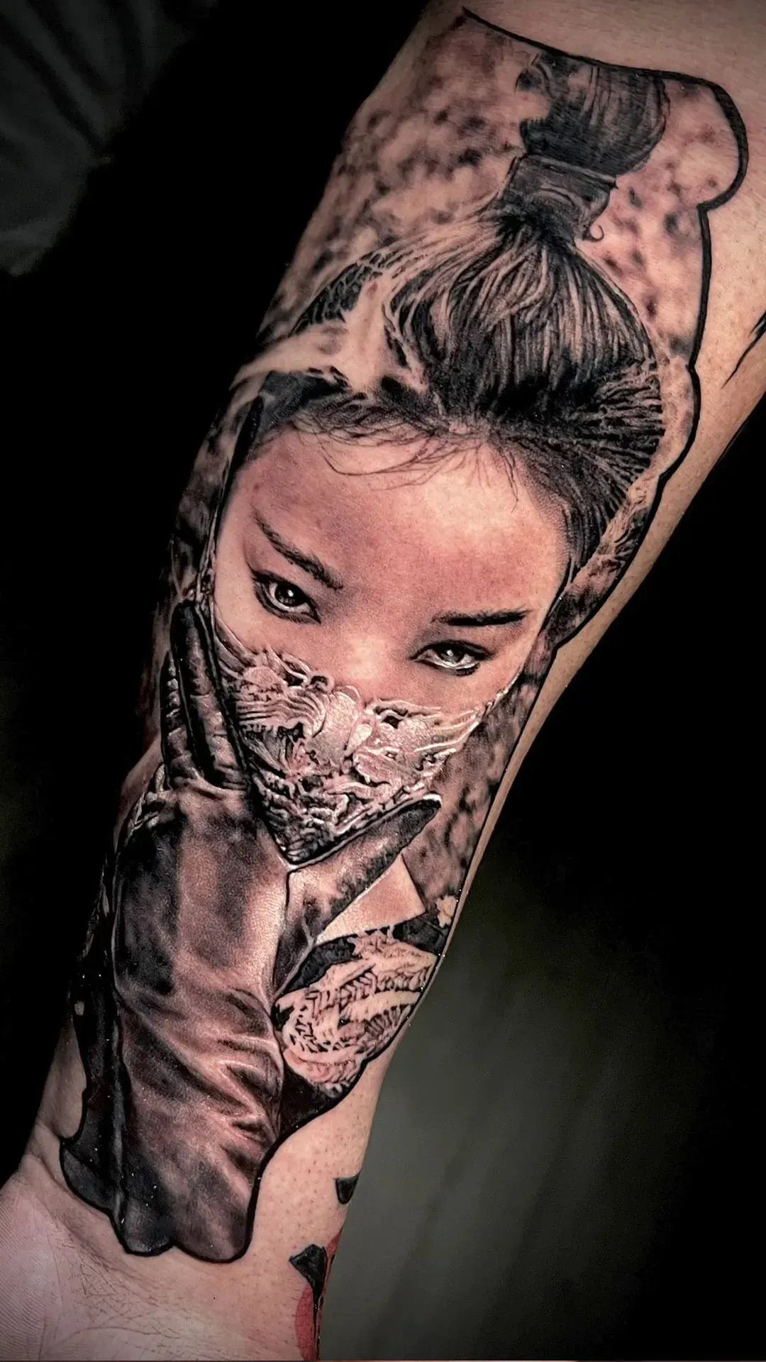 El tatuaje en el brazo representa a una mujer con un cubrebocas estampado y un peinado de moño, en negro y gris.