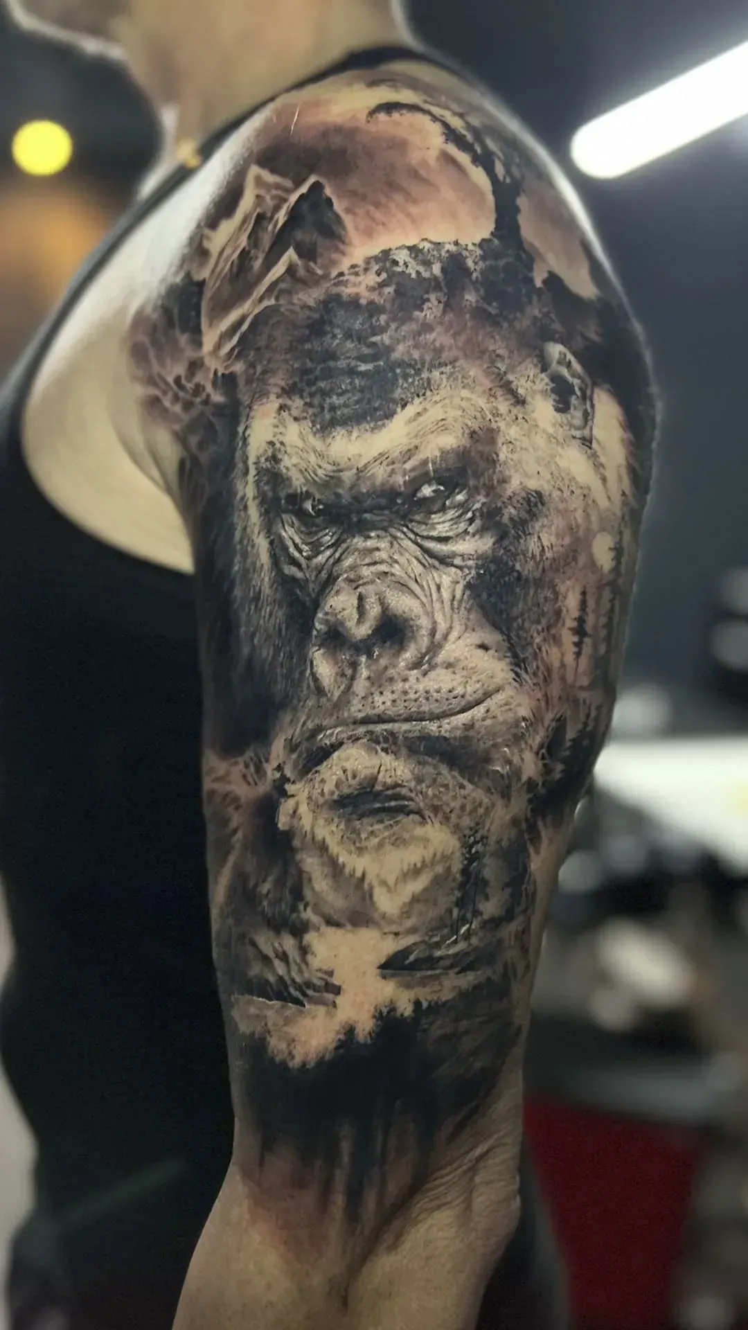Tatuaje de la cara de un gorila en el brazo. El simio es de color oscuro con una escena montañosa al fondo.